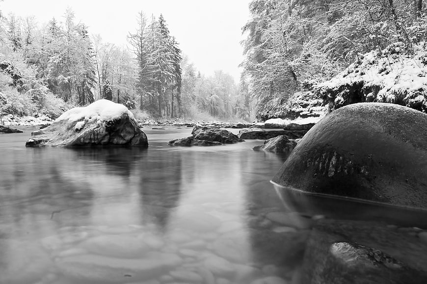Serene black and white winter river landscape with snow-covered rocks