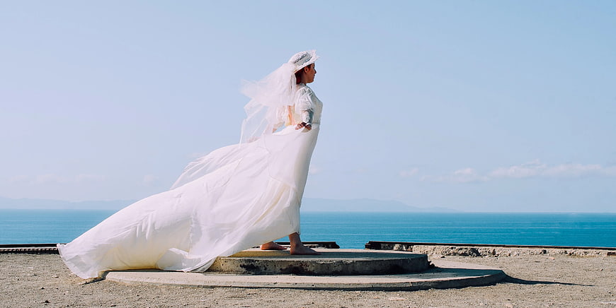 Bride in flowing white gown standing by the ocean