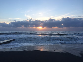 Dramatic sunset over ocean waves with dark clouds and sandy beach