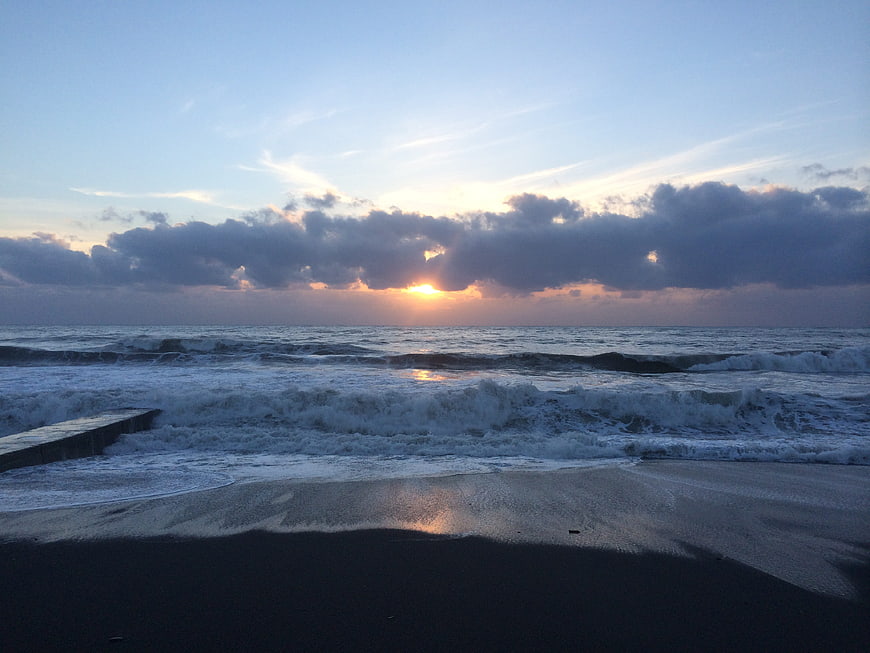 Dramatic sunset over ocean waves with dark clouds and sandy beach