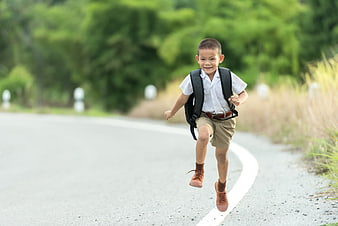 Happy Asian schoolboy running on road with backpack