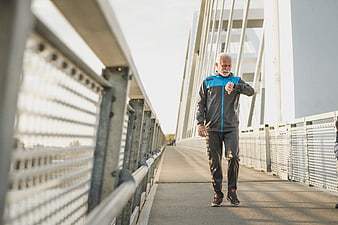 Senior man checking smartwatch while jogging on bridge