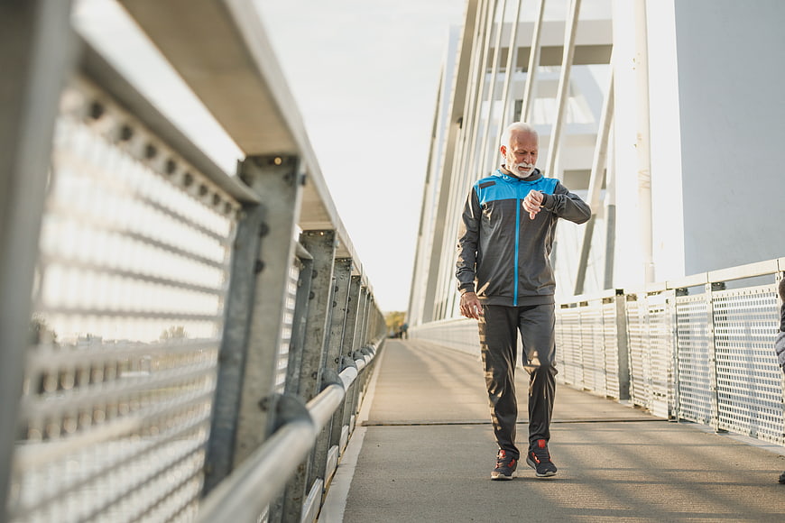 Senior man checking smartwatch while jogging on bridge