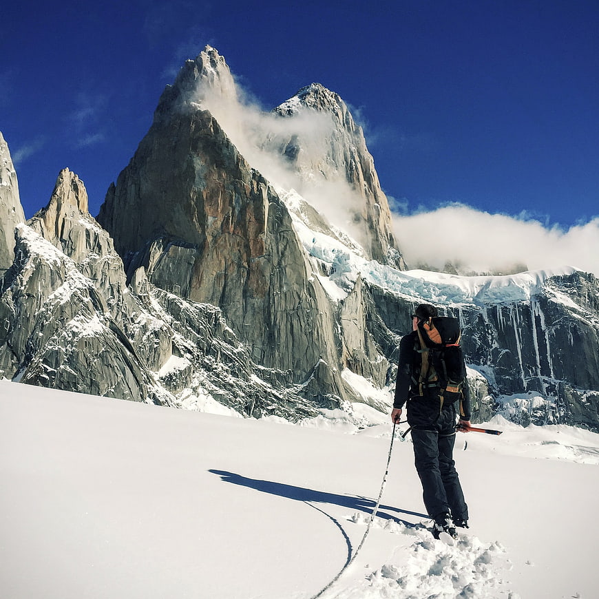 Hiker with Backpack Standing on Snowy Mountain Slope