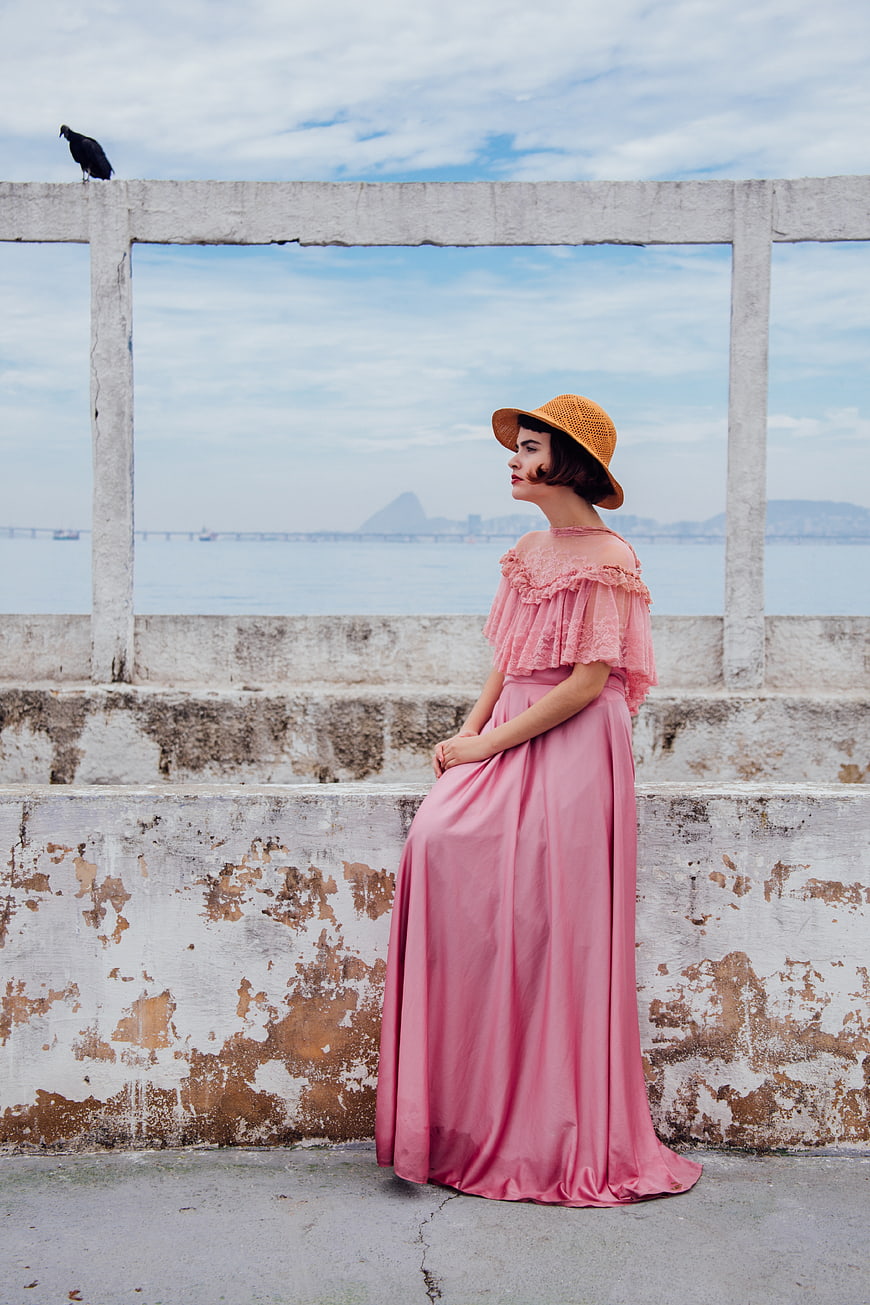 Woman in Pink Dress and Straw Hat by Sea Wall