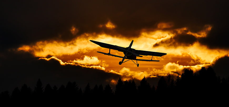 Silhouette of Biplane Flying Against Dramatic Sunset Sky