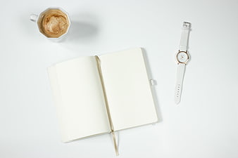 White notebook, coffee cup, and wristwatch on a clean white desk surface