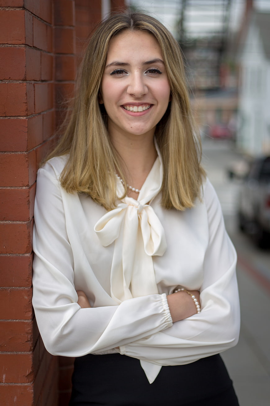 Smiling Business Woman in White Blouse Leaning Against Brick Wall