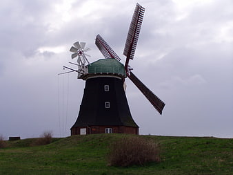 Traditional Black Windmill on Green Hill Under Cloudy Sky