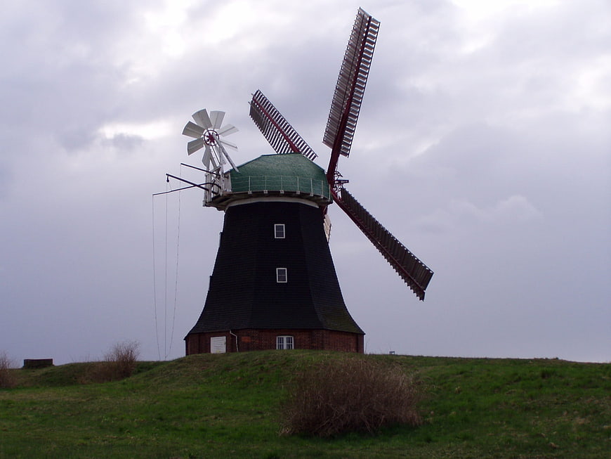 Traditional Black Windmill on Green Hill Under Cloudy Sky