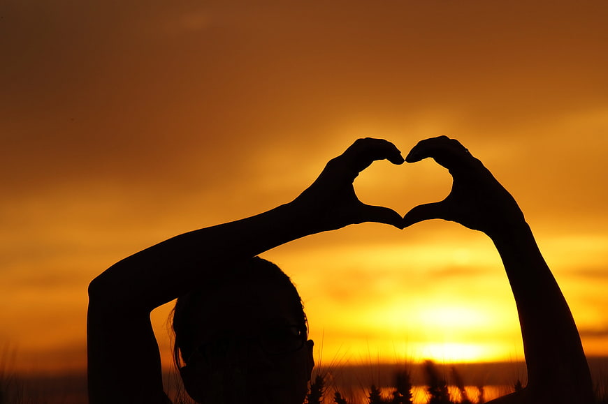 Silhouette of Woman Making Heart Shape with Hands at Sunset