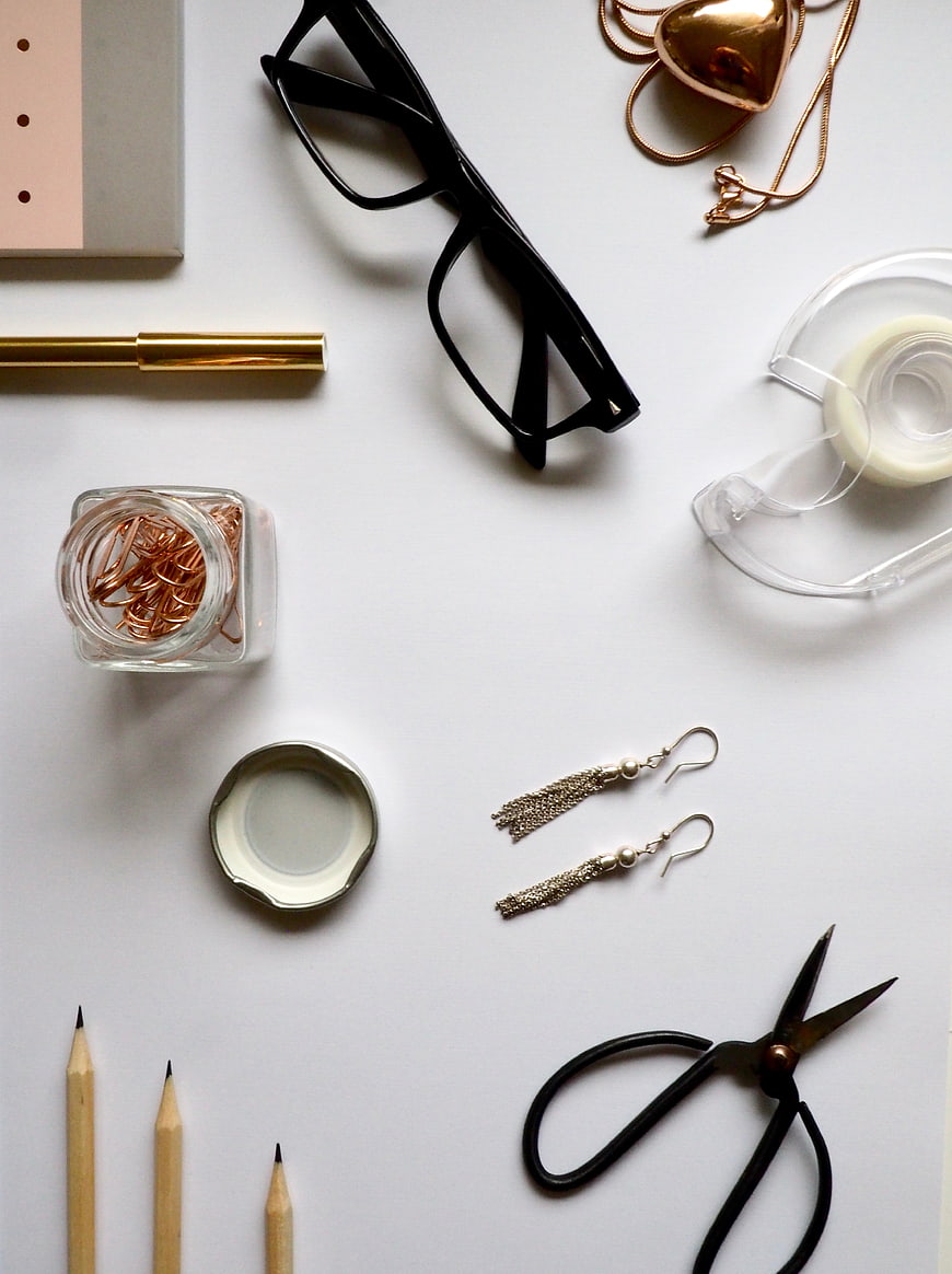 Flat lay of office supplies, jewelry, and stationery on white background