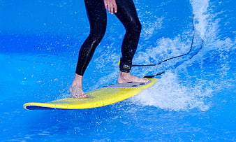 Close-up of surfer legs on yellow surfboard in blue water