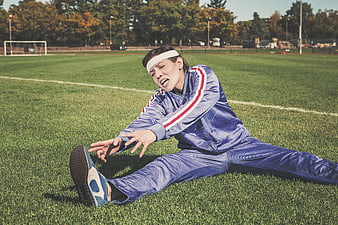 Female athlete stretching on grass field in blue tracksuit