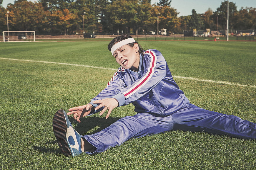 Female athlete stretching on grass field in blue tracksuit