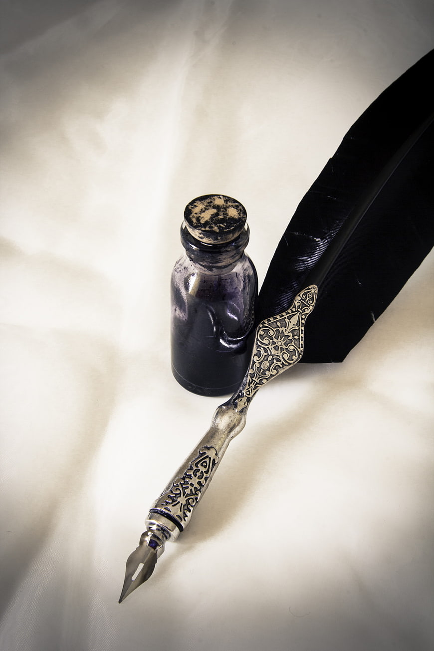Vintage silver quill pen and ink bottle on white fabric
