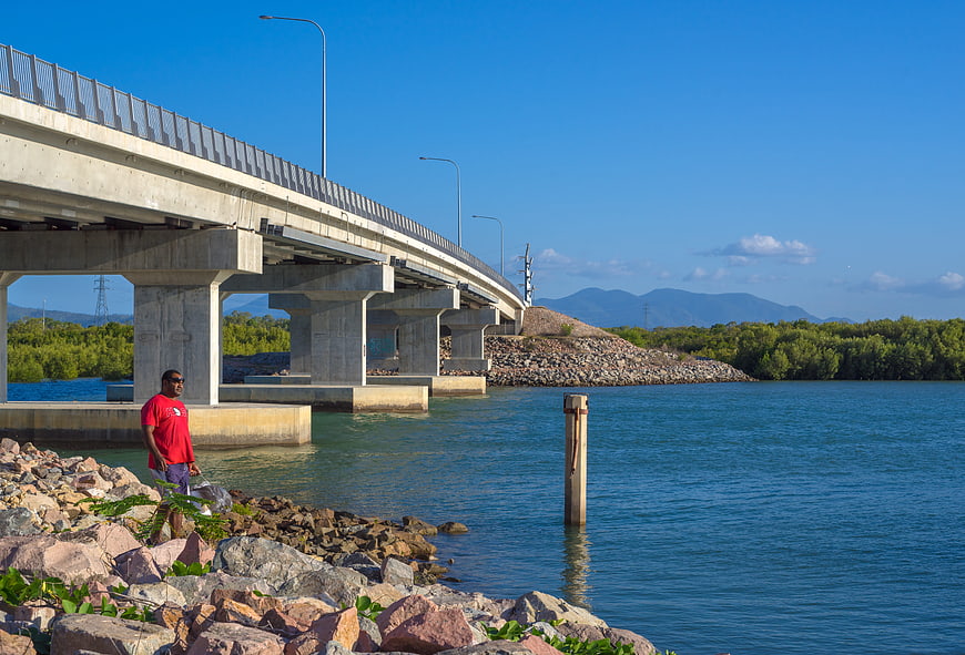 Man fishing under concrete bridge by rocky shore
