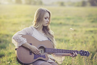 Blonde woman playing acoustic guitar in a sunny field