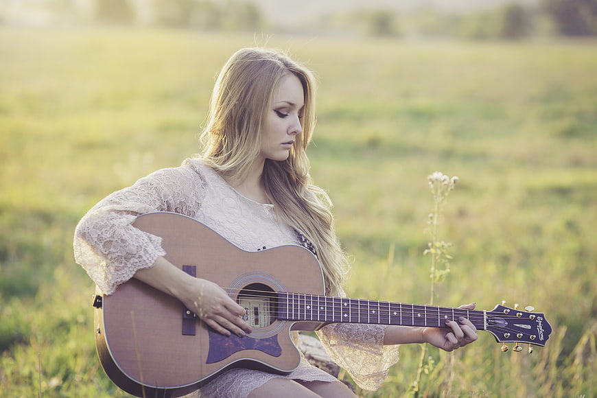 Blonde woman playing acoustic guitar in a sunny field
