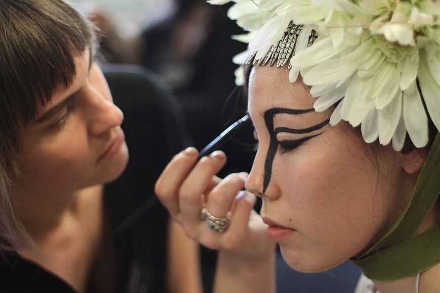 Makeup artist applying dramatic black face paint to model with flower crown