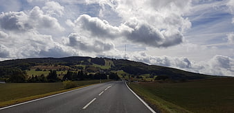 Winding country road through green hills under dramatic cloudy sky