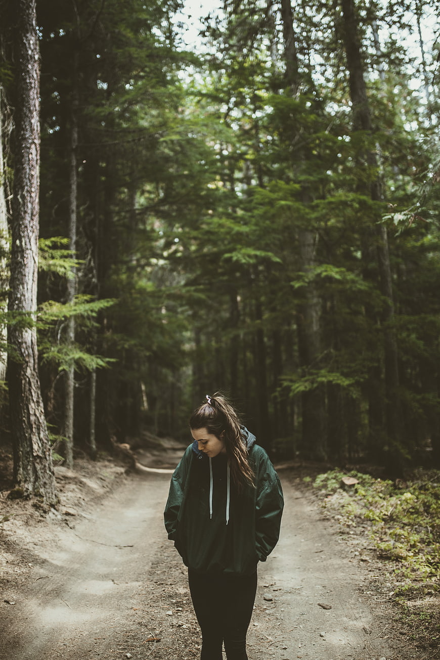 Young woman walking on forest trail in green jacket