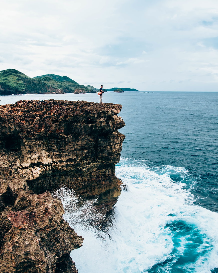 Man standing on rocky cliff edge overlooking ocean waves