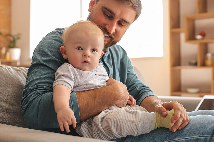 Happy Father Holding Baby on Sofa at Home