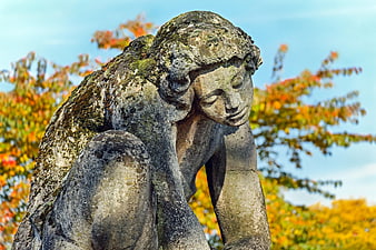 Weathered Stone Statue of a Sorrowful Girl in Autumn Park