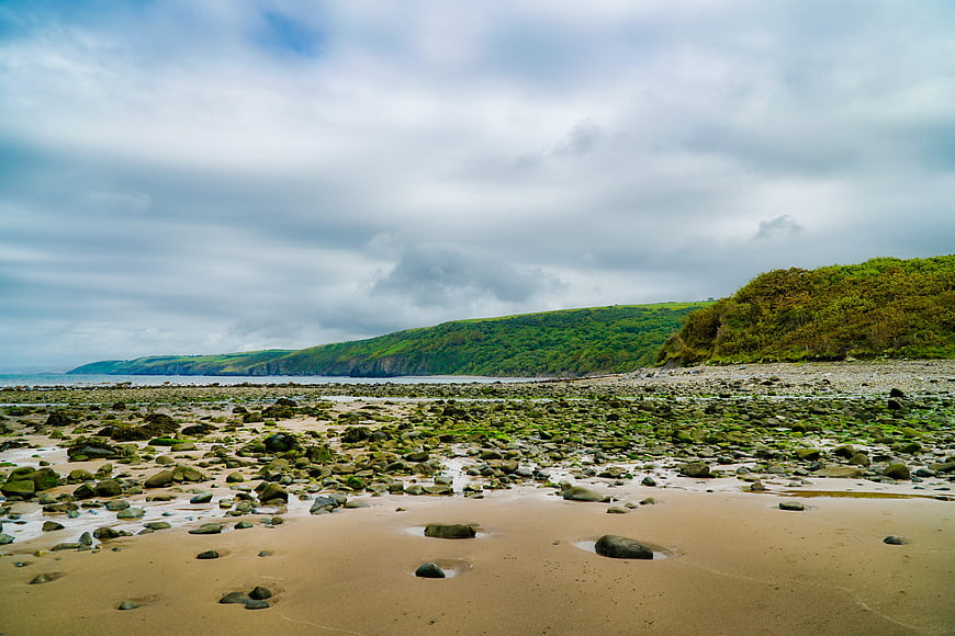 Rocky coastal beach landscape with green cliffs and cloudy sky
