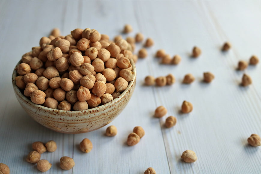 Bowl of dried chickpeas on white wooden background