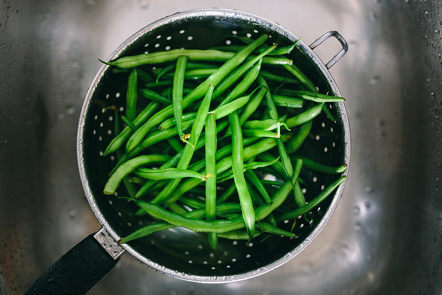 Fresh green beans in metal colander top view