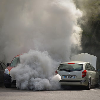 White car emitting thick smoke with open hood in parking lot
