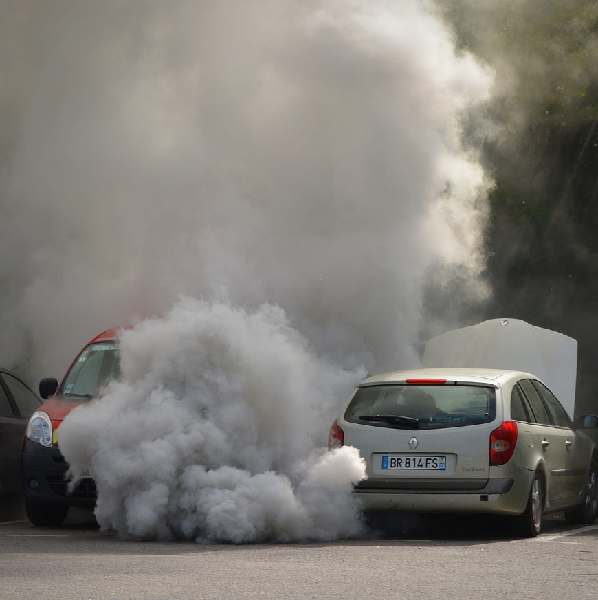 White car emitting thick smoke with open hood in parking lot