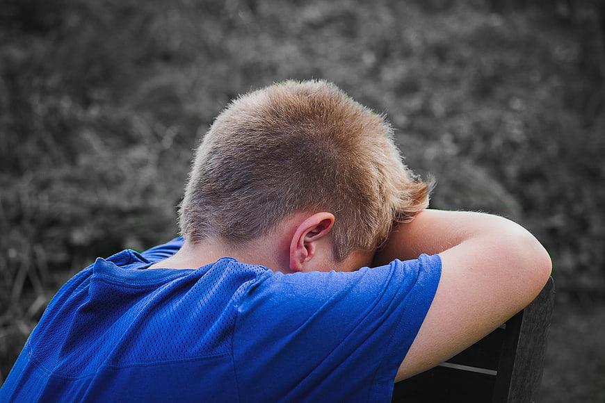 Sad Boy Sitting Alone with Head Down in Blue Shirt