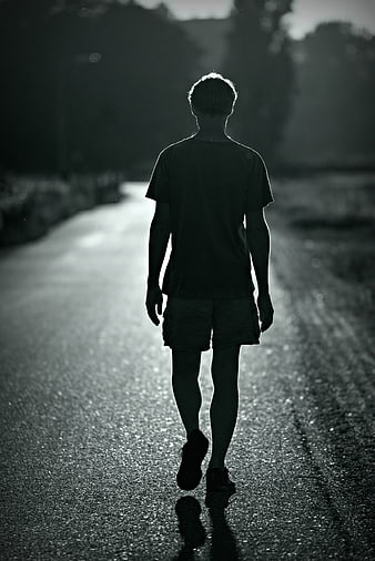 Silhouette of a man walking away on a wet road in black and white