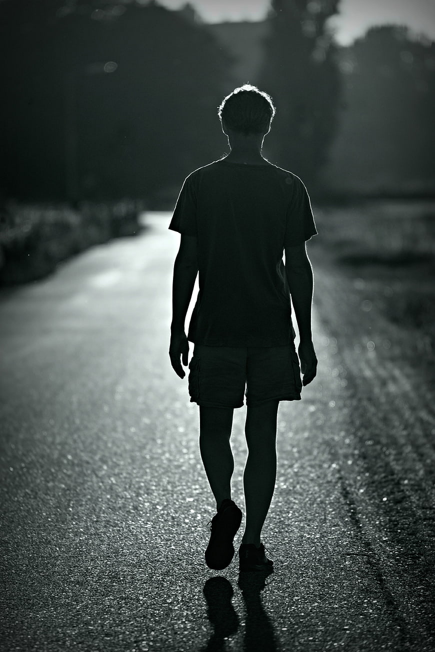 Silhouette of a man walking away on a wet road in black and white