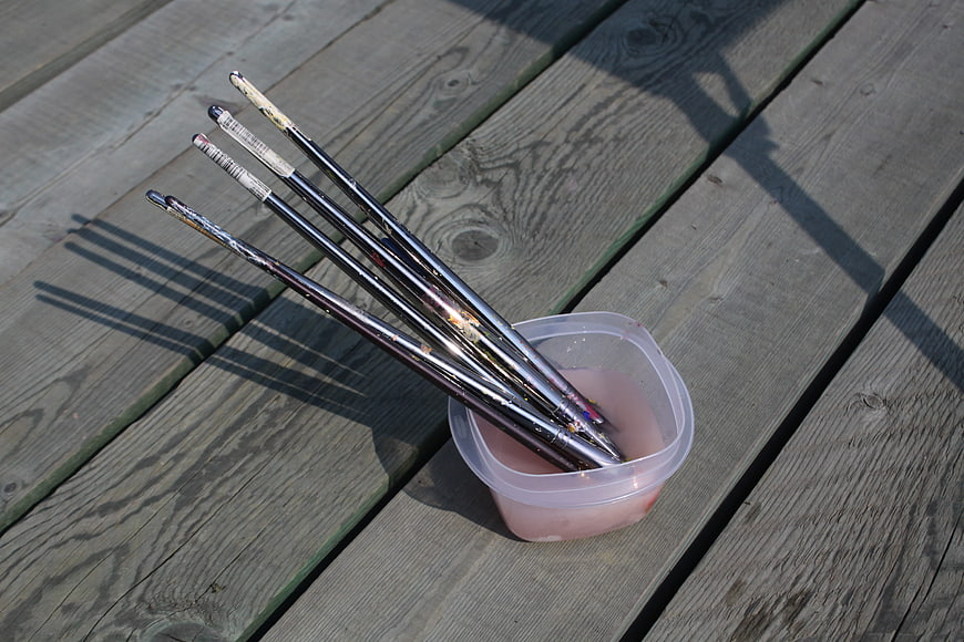 Paintbrushes soaking in water on wooden deck
