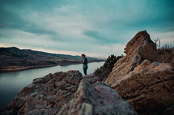 Man standing on rocky cliff overlooking lake at dusk