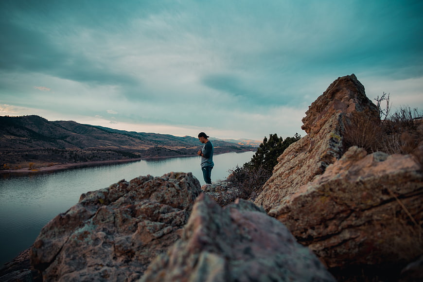 Man standing on rocky cliff overlooking lake at dusk