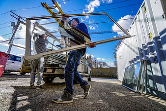 Two Workers Carrying Large Glass Window Panels From Truck