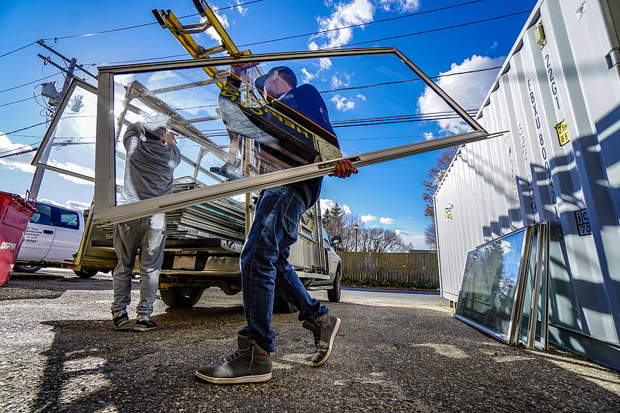 Two Workers Carrying Large Glass Window Panels From Truck