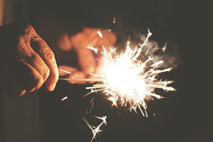 Hands holding a bright sparkler against a dark background