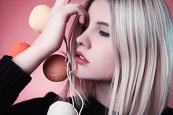 Blonde woman with yarn balls and headphones on pink background