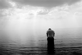 Solitary man standing in water under dramatic cloudy sky