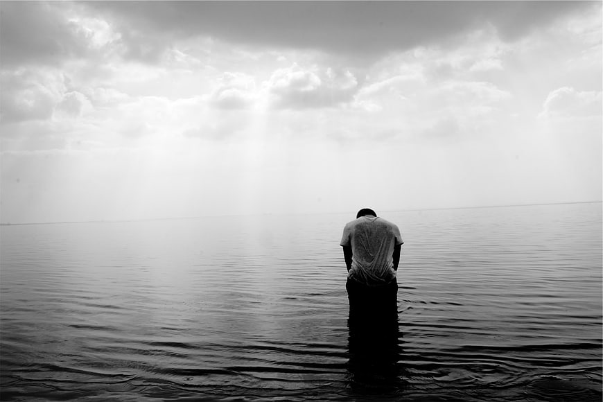 Solitary man standing in water under dramatic cloudy sky
