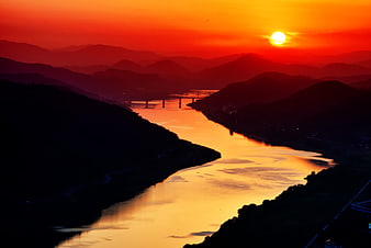 Vibrant red sunset over a winding river and silhouetted mountains