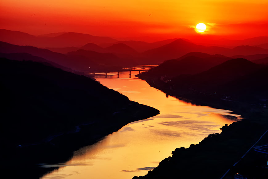 Vibrant red sunset over a winding river and silhouetted mountains