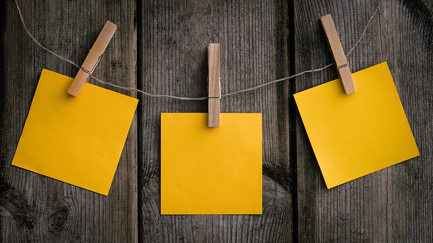 Three yellow sticky notes hanging on a clothesline with wooden clothespins