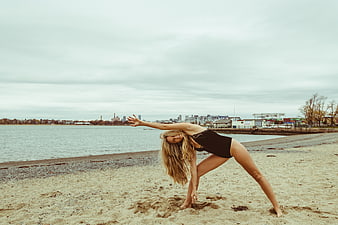 Woman doing yoga on sandy beach with city skyline